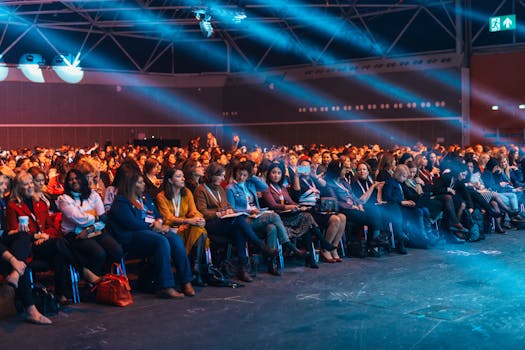 Vibrant image of a diverse audience seated in a large auditorium, highlighted by dynamic stage lighting.